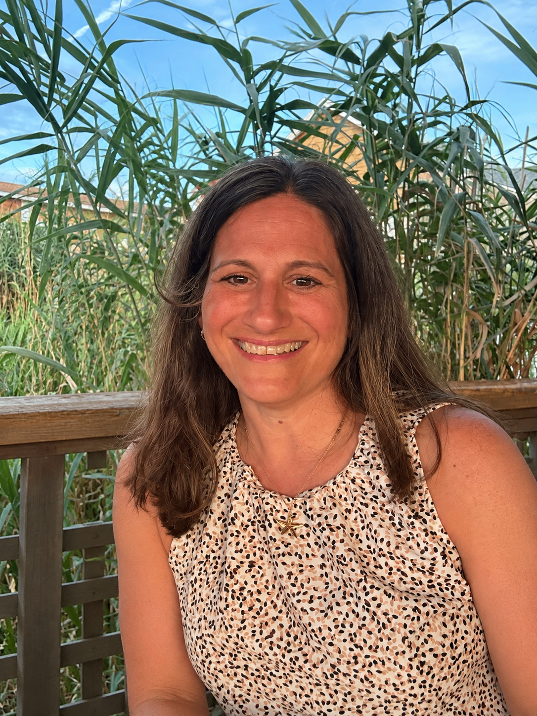 Coach Janine smiling on a deck with marsh grass and blue sky behind her